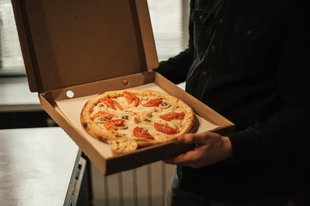 O cutie de pizza deschisă, cu pizza caldă înăuntru, ținută în mâini