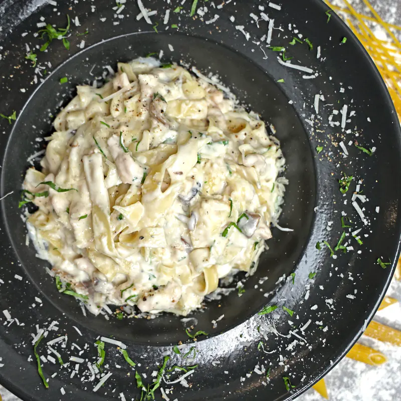 Fettuccine în sos alb cu parmezan, pe o farfurie neagră