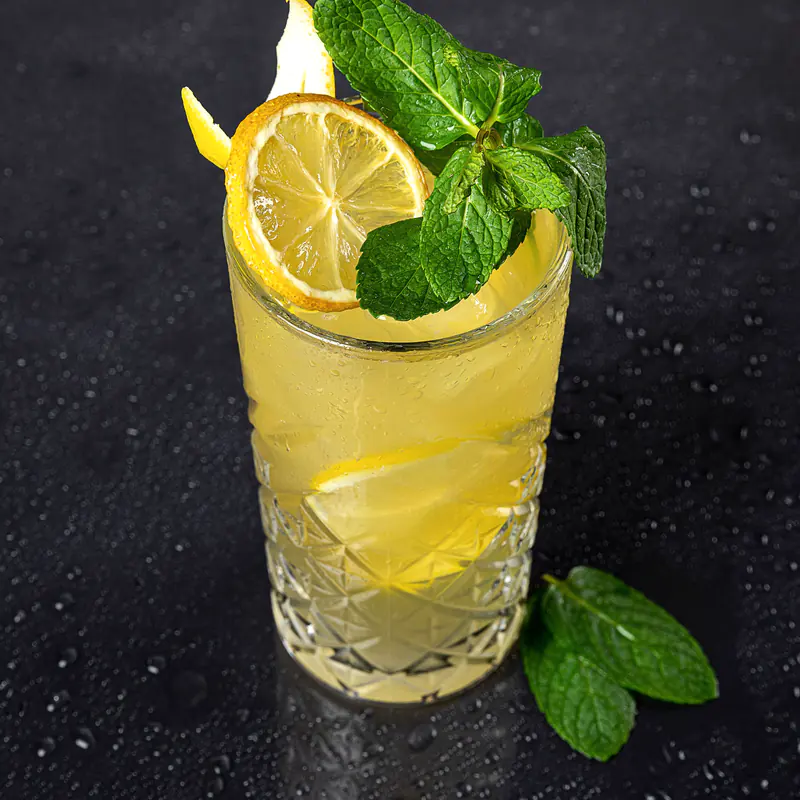 Un pahar înalt cu limonadă, felii de lămâie și mentă