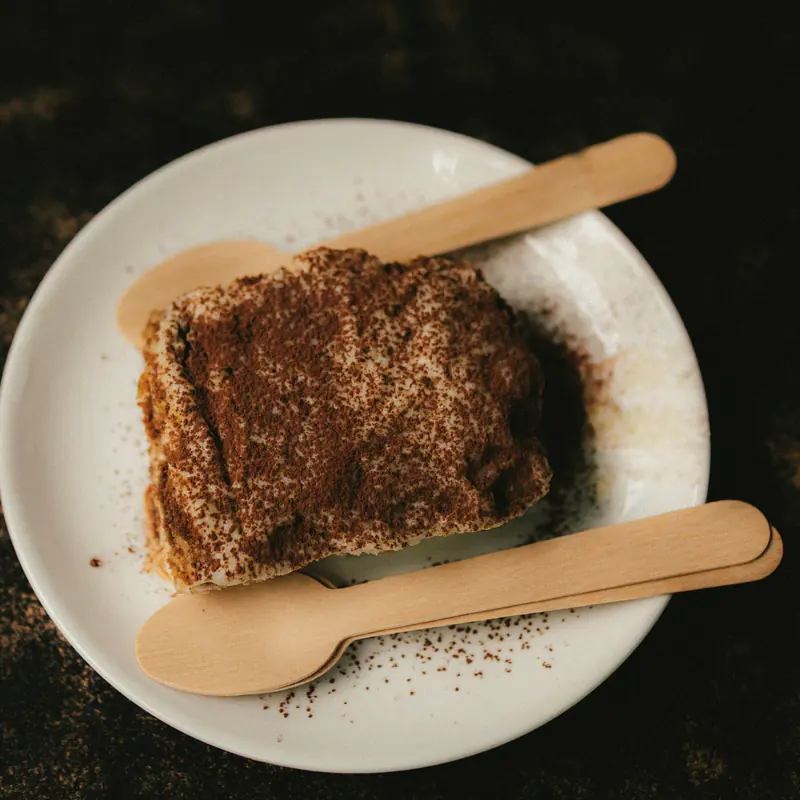 O porție de tiramisu pe o farfurie, cu linguri de lemn